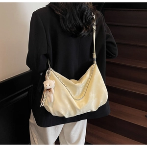 Detail of cream PU leather tote bag with metal chain and plush bear charm on a model