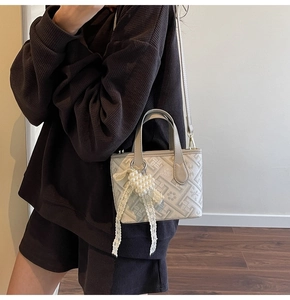 Detail of a grey crossbody bag featuring geometric patterns and a pearl heart charm