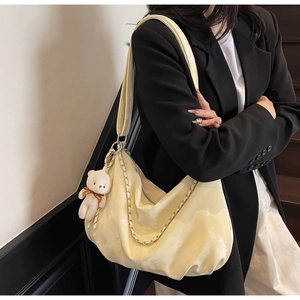 Detail of cream hobo bag with silver chain strap and plush bear charm on model