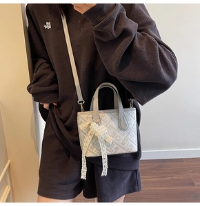 Detail of grey jacquard bucket bag with geometric texture and pearl bow charm