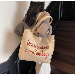 Detailed shot of beige canvas tote bag with red 'less Mondays more Sundays' embroidery