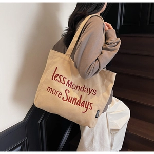 Close-up of beige canvas tote bag with red less Mondays more Sundays embroidery