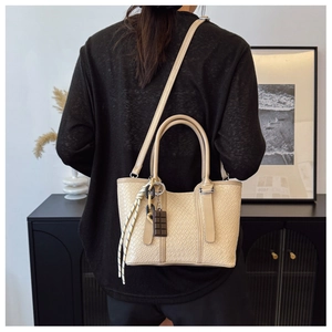 Détail du sac bandoulière beige texturé avec breloque chocolat et cordon tressé chic