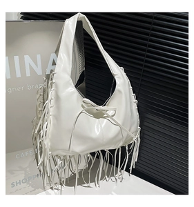 Close-up of white glossy patent leather tote with chic bow detail and long fringe accents