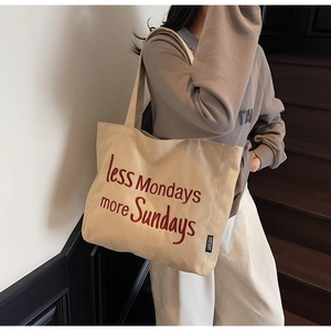 Close-up of beige canvas tote bag with red embroidered text on a female model