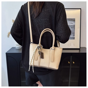 Détail du sac à bandoulière tissé kaki avec poignées cylindriques et breloques de mode