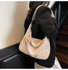 Detail der cremefarbenen Schultertasche mit Blumenstruktur und Bärenanhänger am Model