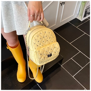 Detail of yellow quilted mini backpack with rhinestone studs and silver chain strap