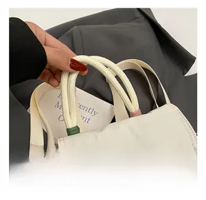 Detail of a beige textured nylon tote bag with colorful MeaRey embroidery and rope handle