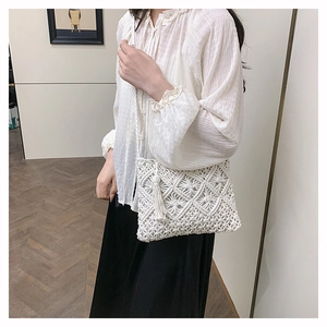 Sac bandoulière en macramé blanc avec pompons et tissage géométrique porté par un mannequin