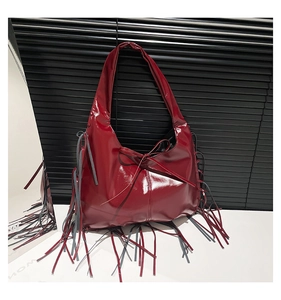 Close-up of a bright red patent leather tote bag with long fringe tassels and a bow detail