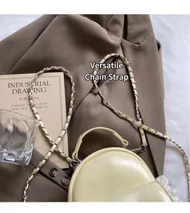 Detailed view of cream PU leather saddle bag with silver metal chain strap on textured surface