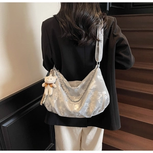 Silver PU tote bag with metal chain detail and plush bear charm shown on model