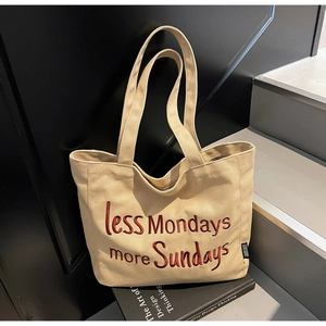 Detail of beige canvas tote bag with red embroidered text on a stack of books