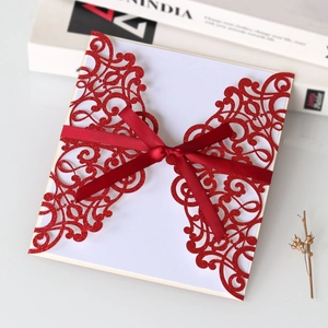 Detail of red glitter laser-cut invitation featuring elegant European vine patterns and silk bow