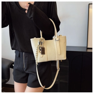 Détail du sac crème avec texture cuir, breloque chocolat et bandoulière tressée