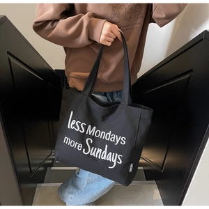 Close-up of black canvas tote bag with white 'less Mondays more Sundays' text embroidery