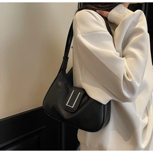 Détail du sac sous l'aisselle en cuir grainé noir avec boucle argentée porté par un modèle
