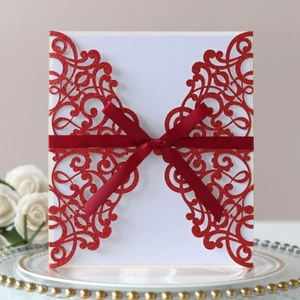 Detail view of laser-cut wedding invitation with red glitter hollow patterns and silk bow