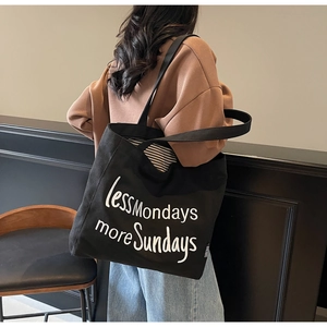Close-up of black canvas tote bag with white less Mondays more Sundays embroidery