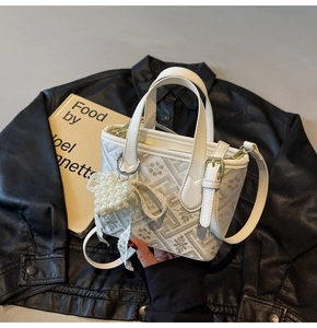 Close-up of a white leather bucket bag with gray floral patterns and pearl bow charm accessory