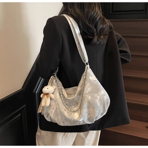 Detailed view of silver metallic shoulder bag with chain strap and teddy bear charm
