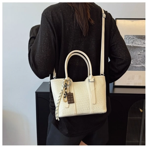 Détail d'un sac à bandoulière beige texturé avec une chaîne élégante et un charme chic