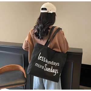 Detail of a large black canvas tote bag with white lettering embroidery and side logo tag