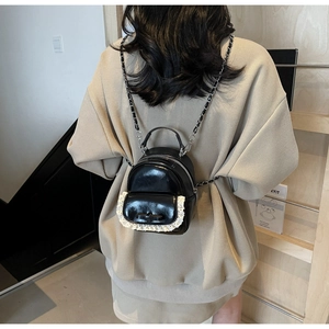 Detail view of a black mini backpack with lace trim, bow, and chain straps on model