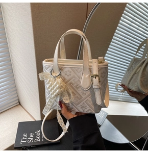 Close-up of beige bucket bag with geometric patterns and a pearl lace bow charm