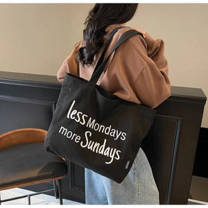 Detail of black canvas tote bag with white less Mondays more Sundays text embroidery