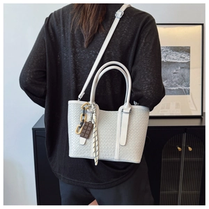 Détail d'un sac à bandoulière blanc texturé avec chaîne dorée et breloque chocolat