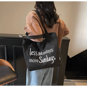 Close-up of black canvas tote bag with white less Mondays more Sundays letter print