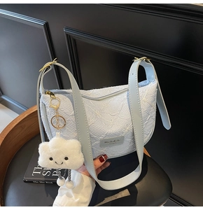 Detail of light blue crescent bag with white jacquard texture and cloud plush charm