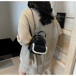 Close-up of a mini black leather backpack featuring lace edges and bow detail on model