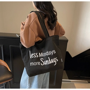 Close-up of black canvas tote bag featuring less Mondays more Sundays white embroidery text