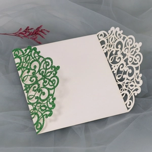 Detail of laser-cut wedding invitation with green glitter vine and cream floral patterns
