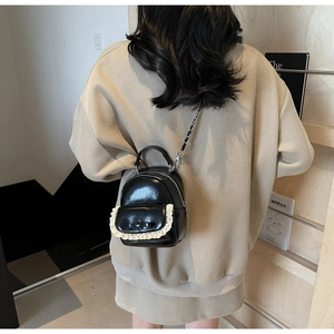 Detail of mini black patent leather backpack with lace trim and bow on a model