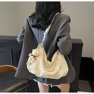 Detail view of cream crossbody bag with silver chain and plush bear charm on model