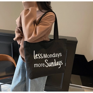 Close-up of black canvas tote bag with 'less Mondays more Sundays' white text embroidery