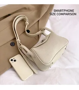 Detail view of beige lychee leather bag with silver lock next to smartphone for size