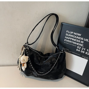 Detail of black glossy leather shoulder bag with silver chain and cute bear charm