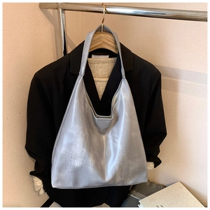 Detail of silver metallic tote bag with wide strap hanging against clothing background