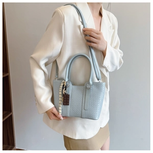 Détail du petit sac bandoulière bleu clair tissé porté avec un blazer blanc élégant