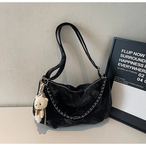 Detail of black glossy pleated shoulder bag with silver chain and white teddy bear charm