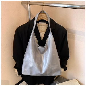 Detail of silver metallic tote bag hanging on a wooden hanger against a black blazer