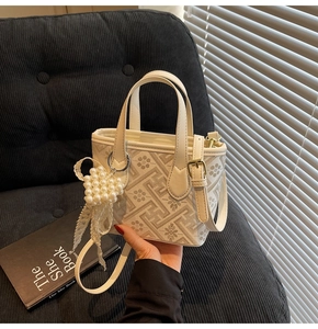 Detail of cream bucket bag with geometric flower print, pearl heart, and lace bow charms