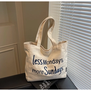 Detail showing beige canvas tote bag with blue 'less Mondays more Sundays' text embroidery