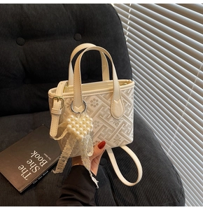 Detail of cream crossbody bucket bag with floral patterns, pearl heart charm and lace bow