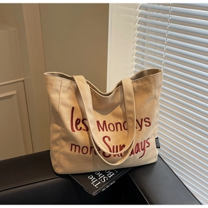 Close-up of beige canvas tote with red embroidery lettering and thick fabric straps